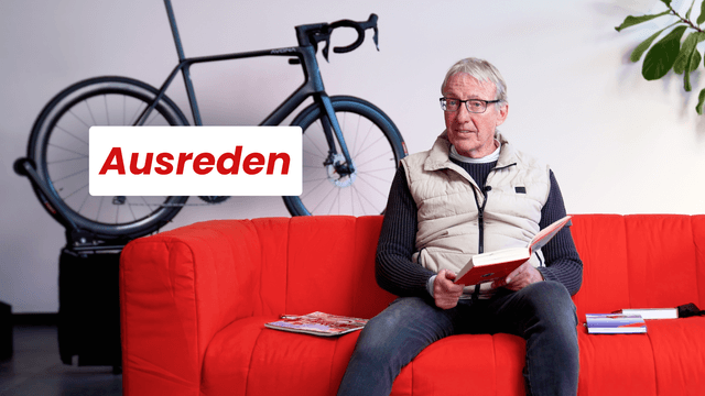 A man sits on a red sofa reading a book, with the word "Ausreden" and a bicycle in the background.